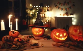 Halloweenska výzdoba v podobe halloweenských tekvíc na jedálenskom stole. Vedľa tekvíc horia sviečky a v pozadí je krb, nad ktorým visia malé oranžové a čierne vlajky.