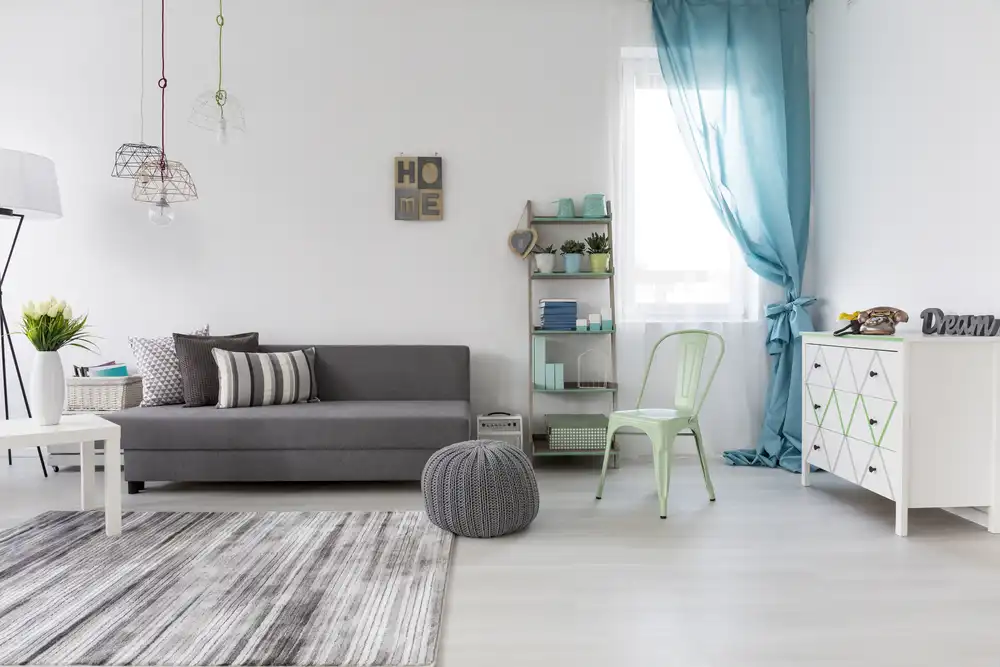 Svetlá obývačka so sivou pohovkou, zelenou stoličkou a modrými závesmi, ktorá kombinuje pohodlie s čistými farbami pre pokojnú atmosféru.