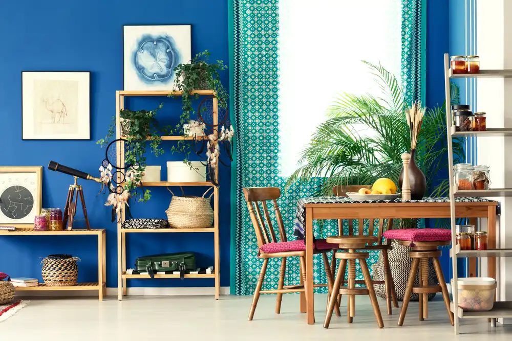 Jasne modrá stena obývacej izby v boho štýle s dreveným nábytkom, farebnými textíliami a dekoráciami s rastlinnými motívmi.