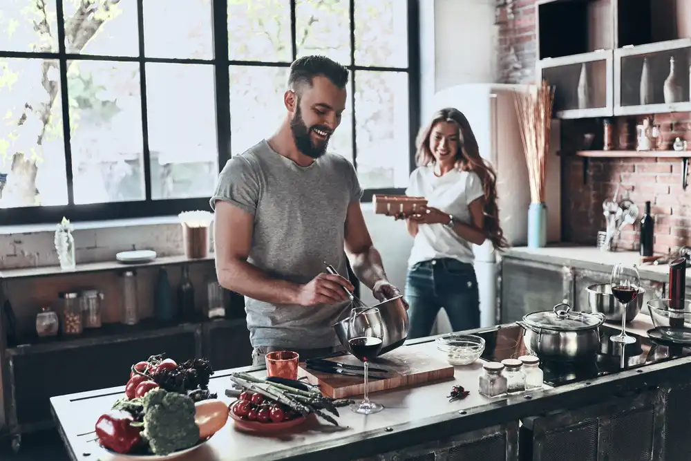 Muž a žena pripravujú jedlo v modernej kuchyni, muž mieša ingrediencie v mise a žena sa smeje.