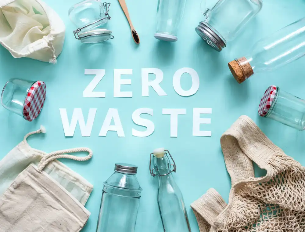 Rôzne opakovane použiteľné a udržateľné predmety ako sú sklenené fľaše, plátené tašky a bambusový zubný kefka na modrom pozadí s textom "ZERO WASTE".