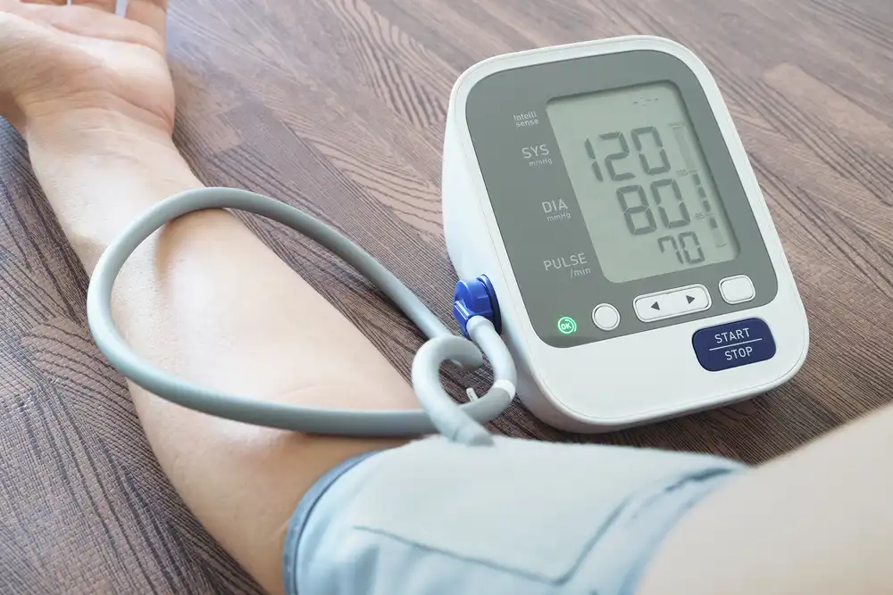 Tlakomer ukazujúci normálne hodnoty krvného tlaku na displeji, vedľa ktorého je ruka pacienta, symbolizujúci úspešnú kontrolu a udržiavanie krvného tlaku v normálnych medziach.