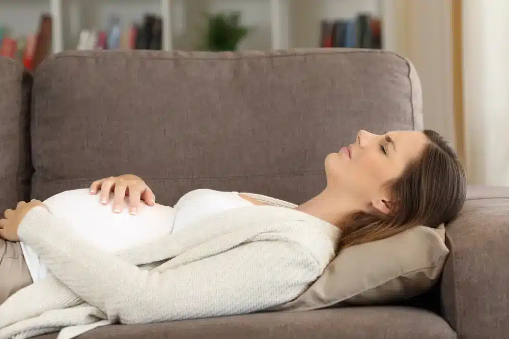 Tehotná žena ležiaca na pohovke s rukami na bruchu.