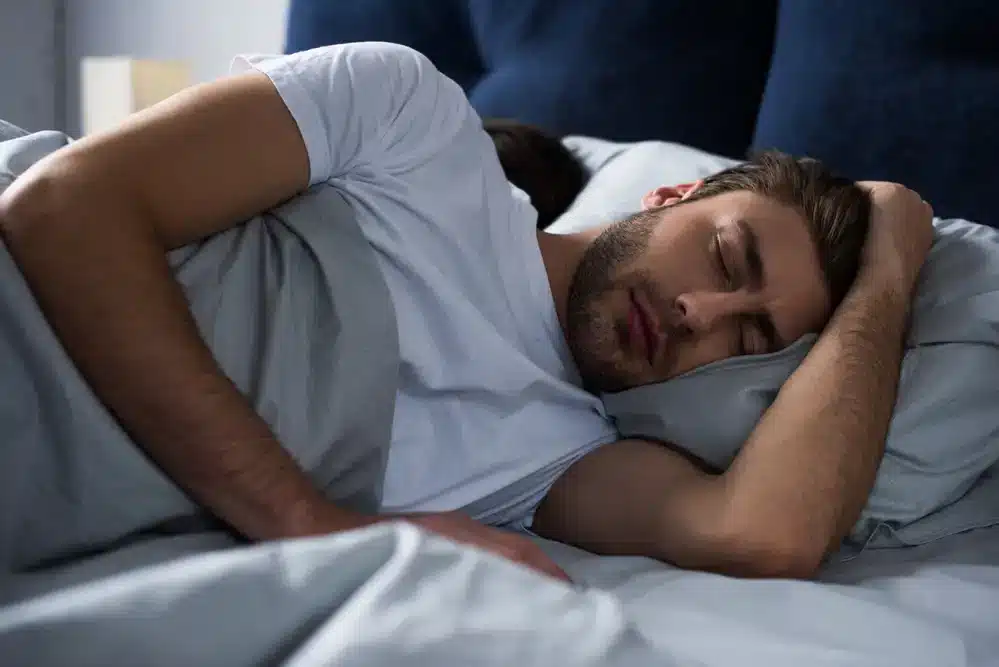 Muž spiaci pokojne na boku v posteli, v nočnej atmosfére, symbolizuje pohodlie a hlboký spánok.
