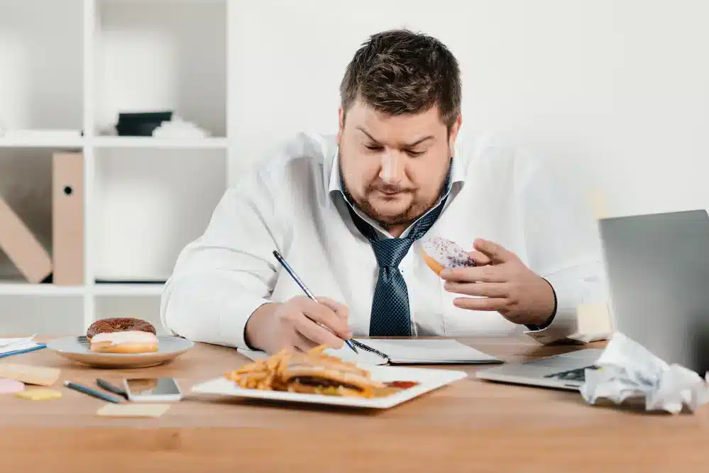 Muž konzumujúci nezdravé jedlo, ktoré môže viesť k zvýšeniu hladiny cholesterolu.