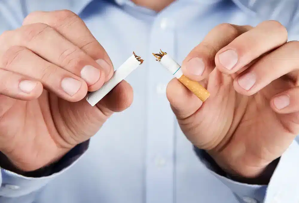 Ruky muža lámu cigaretu na polovicu, symbolizujúce rozhodnutie prestať fajčiť.