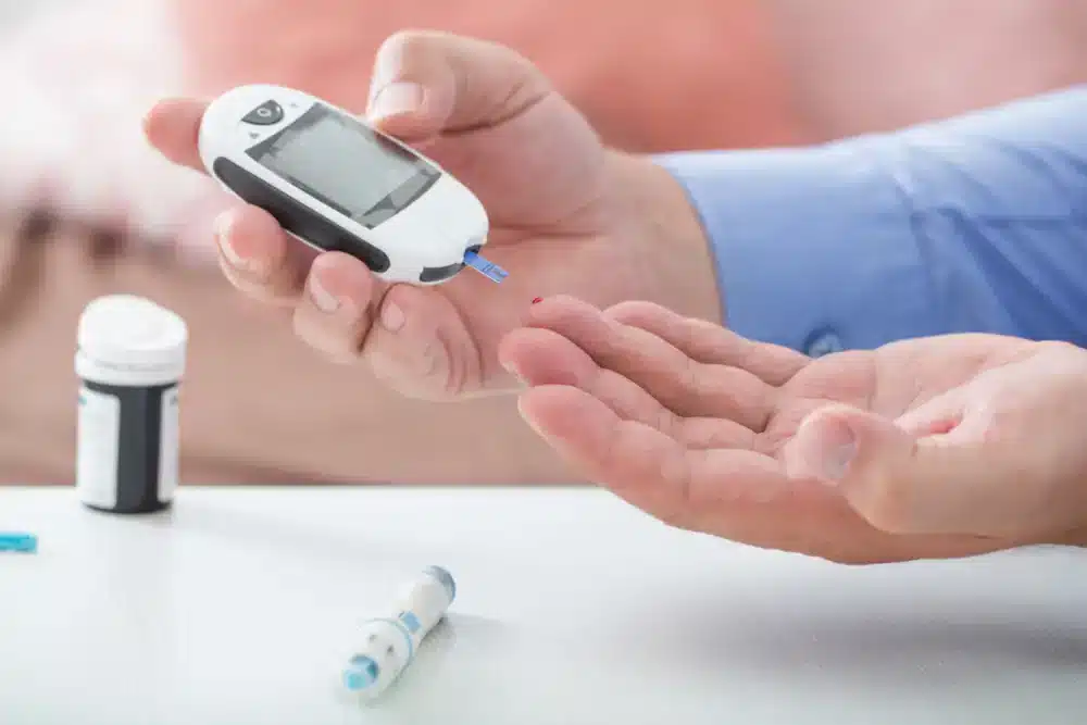Osoba drží glukometer a pripravuje sa na meranie hladiny cukru v krvi, čo je dôležitý krok pre správu diabetu.