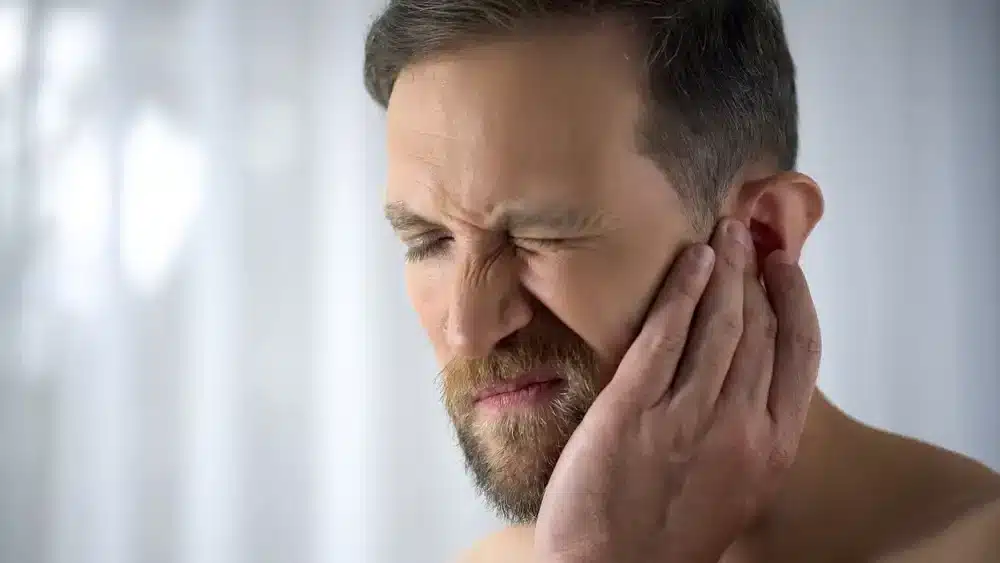 Muž si masíruje oblasť ucha a čeľuste, čo je technika, ktorá môže zmierniť nepohodlie spôsobené tinnitom a napomôcť cirkuláciu v tejto oblasti.