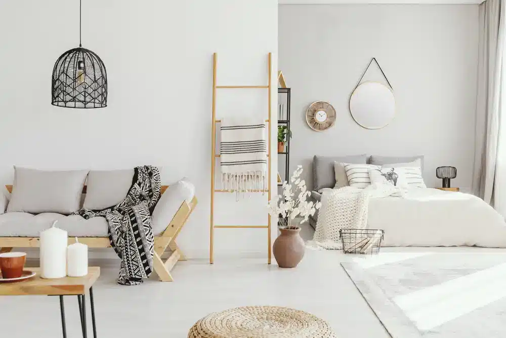 Obrázok zobrazuje obývačku s minimalistickým dizajnom. Biele steny, jednoduchý drevený nábytok a neutrálna farebná schéma vytvárajú pocit priestoru v malom byte. Detaily ako vzorovaná deka a keramická váza pridávajú textúru a osobnosť.