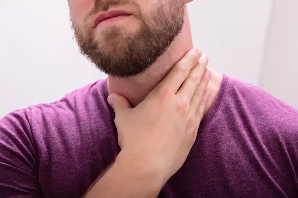 Muž sa dotýka krku, čo môže signalizovať bolesť v krku alebo problémy s prehĺtaním spojené s chronickou bronchitídou.