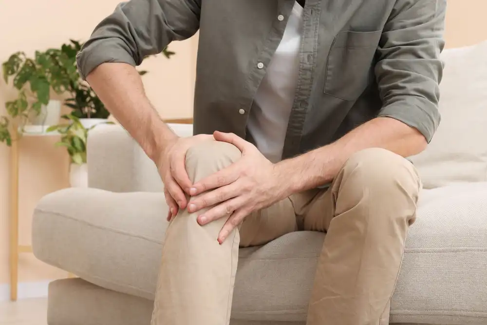 Muž sediaci na gauči drží rukou koleno, zdá sa, že ho bolí.