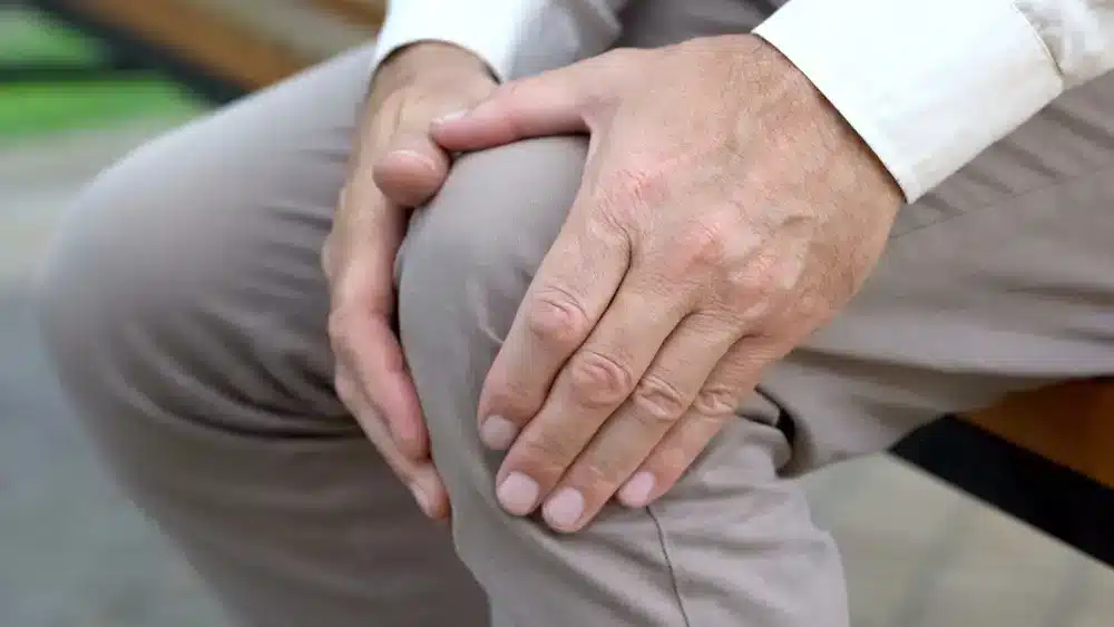 Starší muž sedí a drží si rukou koleno, čo môže byť znakom bolesti spôsobenej dnou.