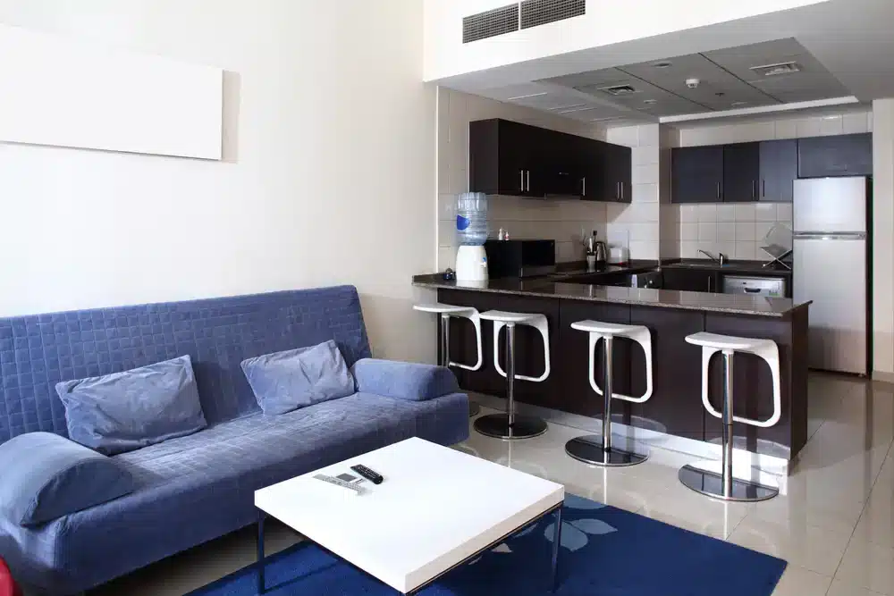 Funkčné rozloženie malého bytu s modrou pohovkou a kuchynským pultom slúžiacim ako jedálenský stôl, čo je praktické riešenie pre byt 2+kk.