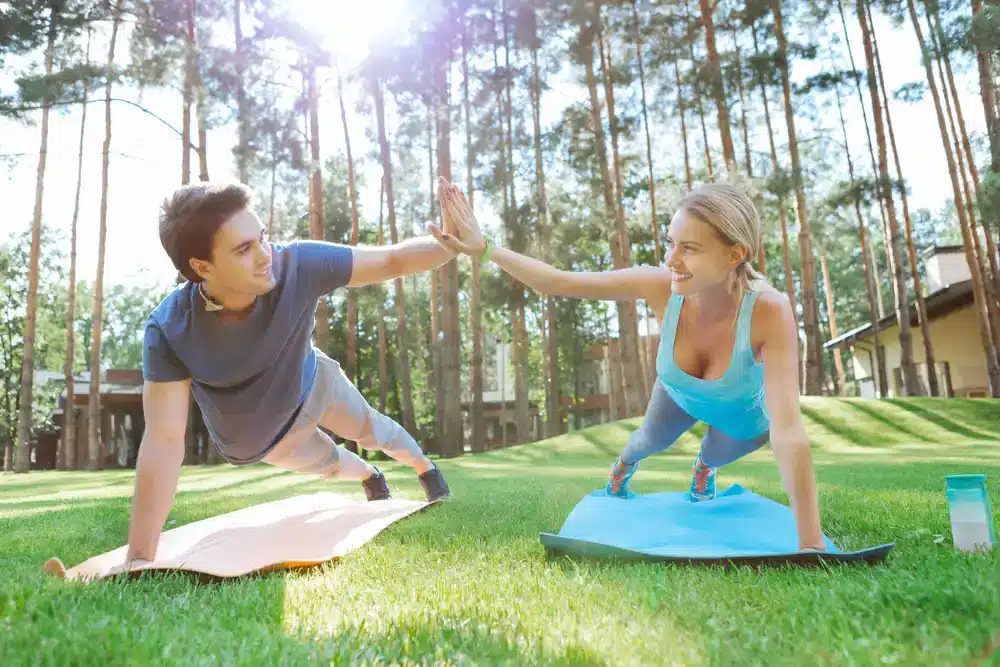 Dvojica robí plank na joga podložkách vonku, ukážka vysoko intenzívneho intervalového tréningu pre zvýšenie metabolickej rýchlosti.