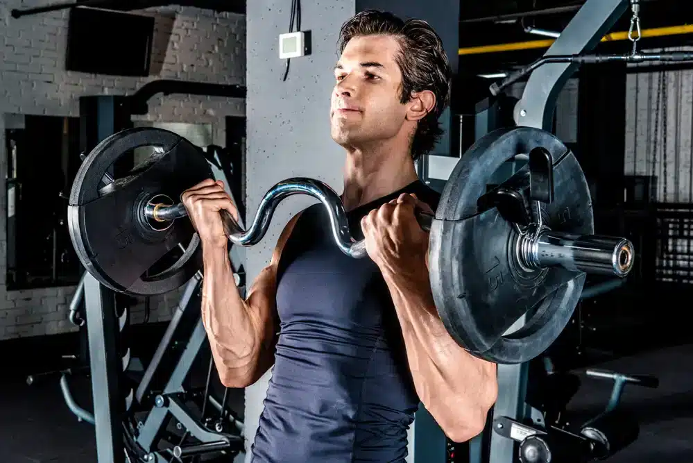 Muž dvíha činky v posilňovni, príklad anaeróbneho cvičenia, ktoré zvyšuje svalovú hmotu a podporuje metabolizmus.
