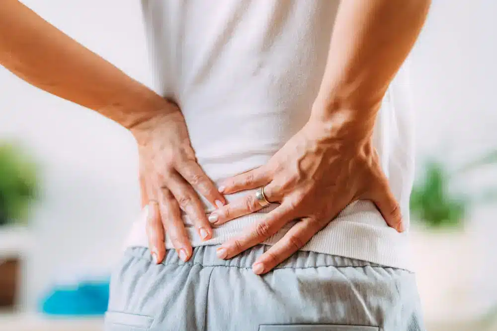 Žena stojaca a držiaca sa za chrbát kvôli bolesti, čo môže signalizovať ischias alebo zápal sedacieho nervu.