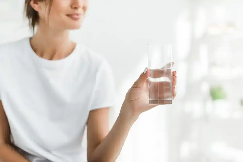 Žena drží pohár vody, čo pripomína, že pitie studenej vody môže urýchliť metabolizmus.