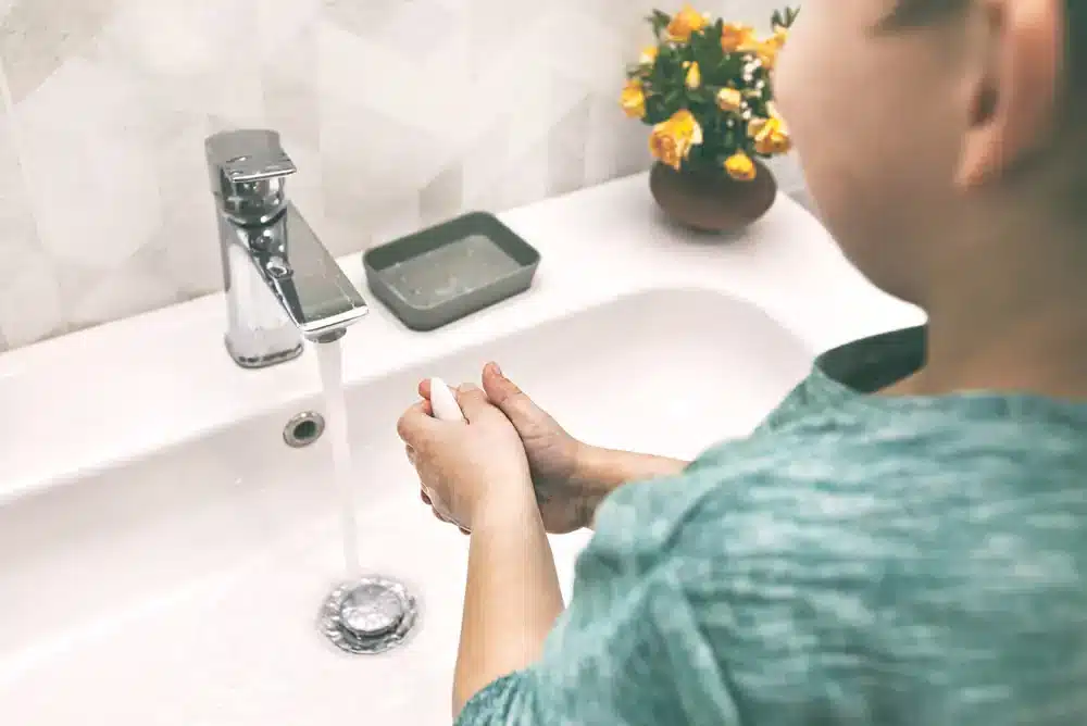 Dieťa si umýva ruky pod tečúcou vodou v umývadle, čo zdôrazňuje dôležitosť osobnej hygieny.