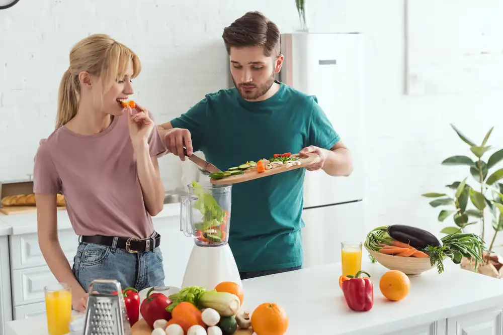 Mladý pár pripravuje smoothie z čerstvej zeleniny – zdravé stravovanie v rámci biohackingu.